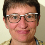 Portrait souriant d'une femme aux cheveux courts et aux lunettes, devant un mur clair.