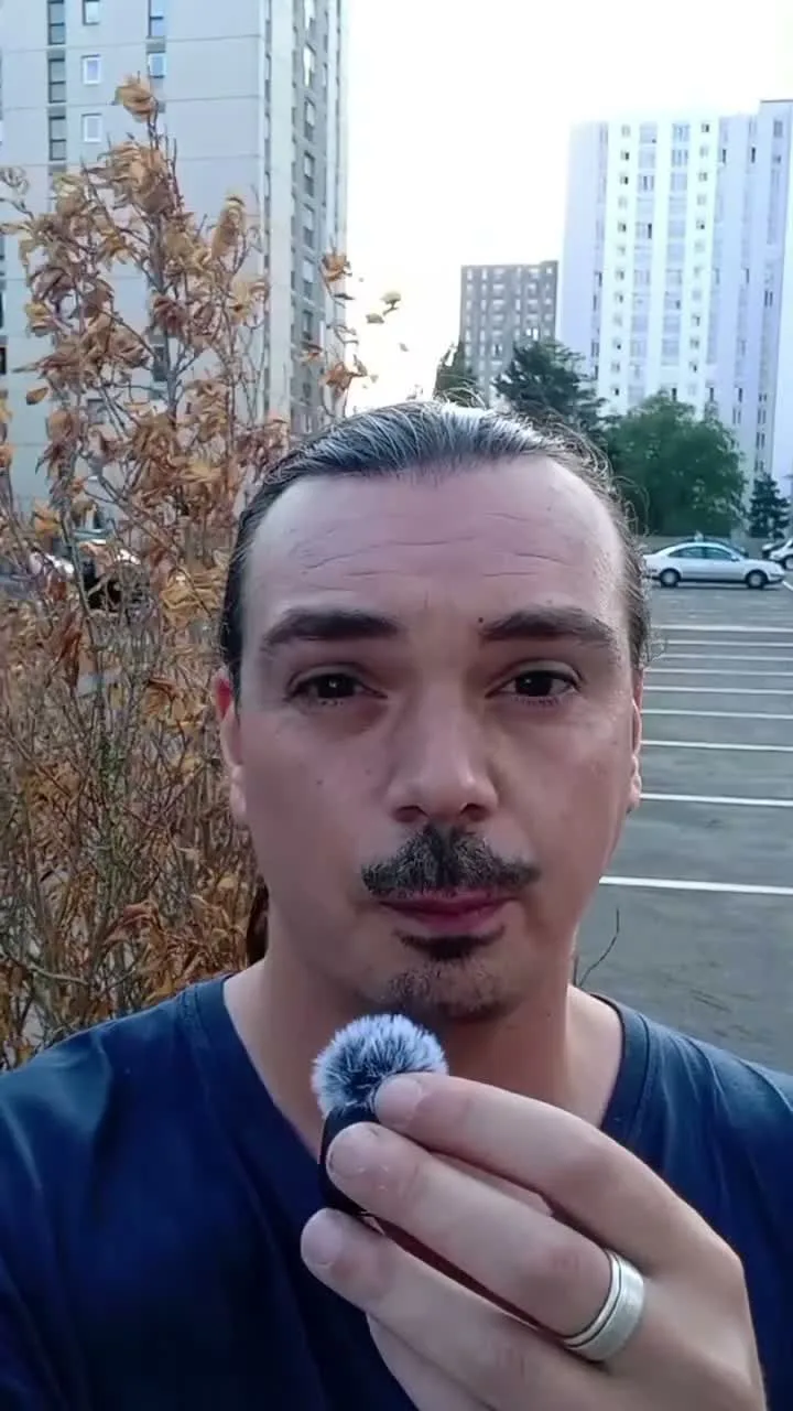 Benjamin Burlon parle face à la caméra, micro-cravate à la main, devant les tours d’un ensemble de logements et un parking, à Antony.